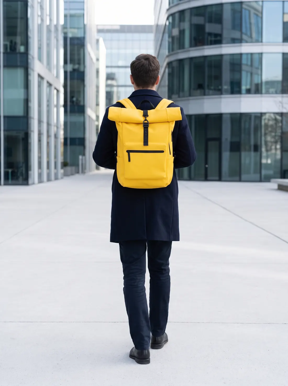 Una persona de espaldas cruza una plaza de oficinas con la mochila Pilatus Urban amarilla